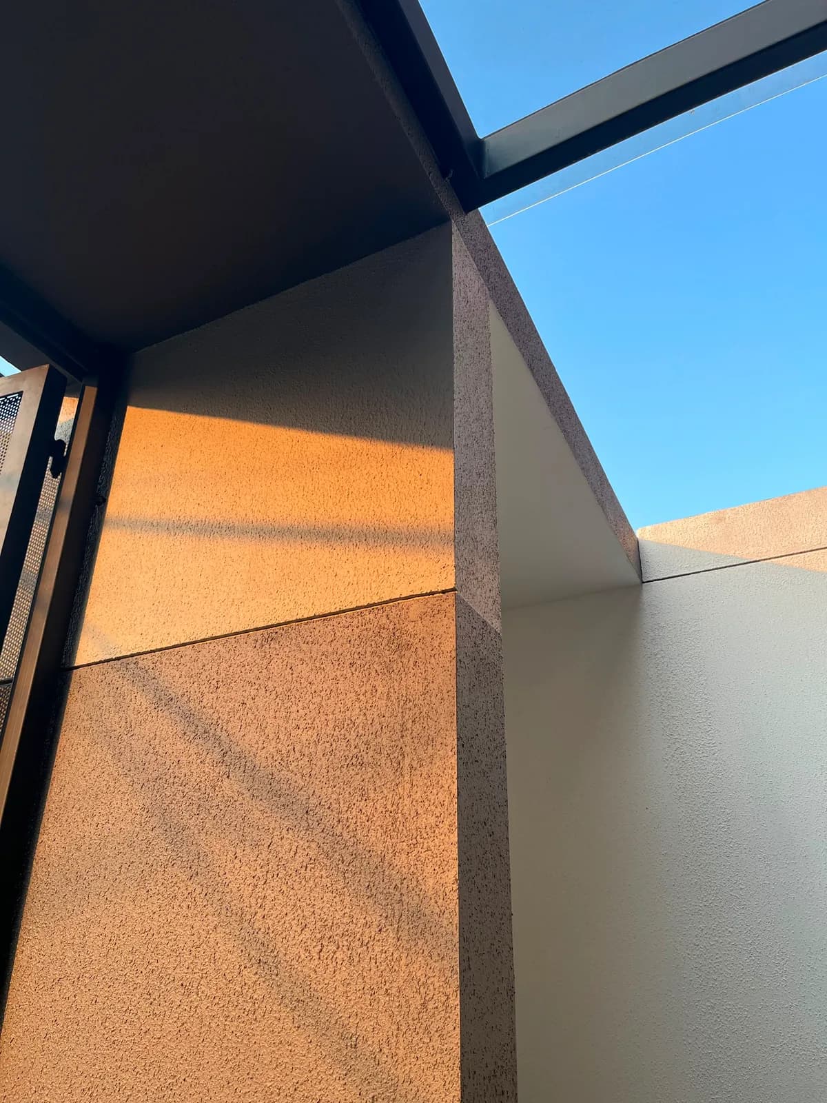Corner of the textured plaster wall meeting the black steel canopy beam against a clear sky