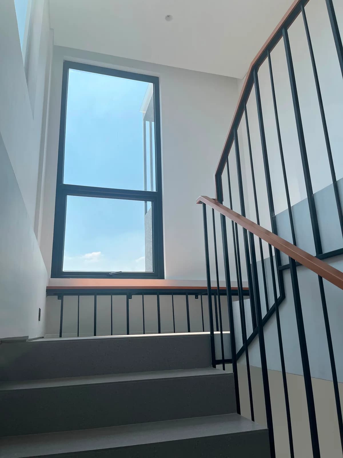 Staircase with grey terrazzo steps, a black steel balustrade and a timber handrail