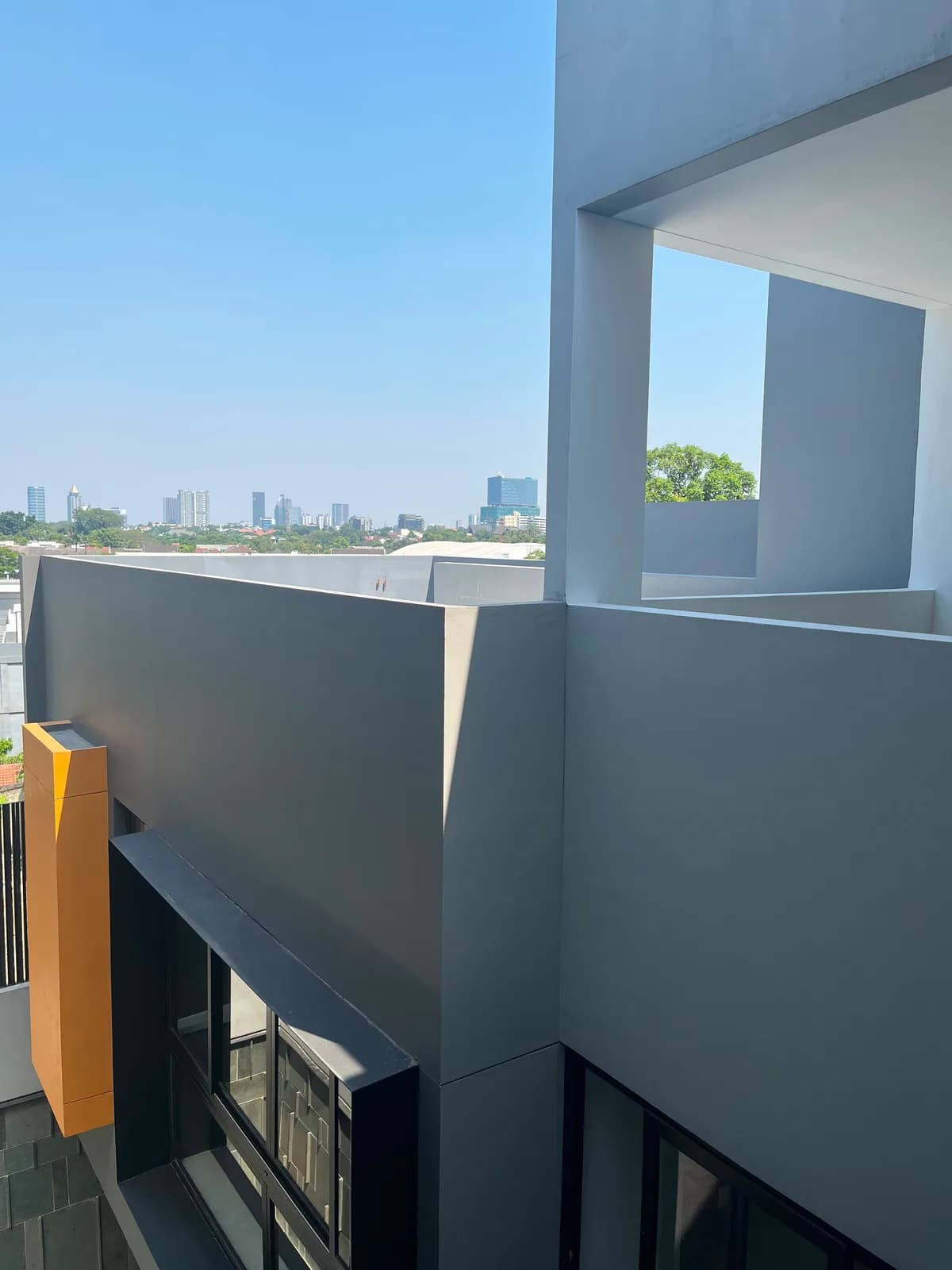 Grey plastered walls and the orange projecting box at roof level, with the city skyline behind