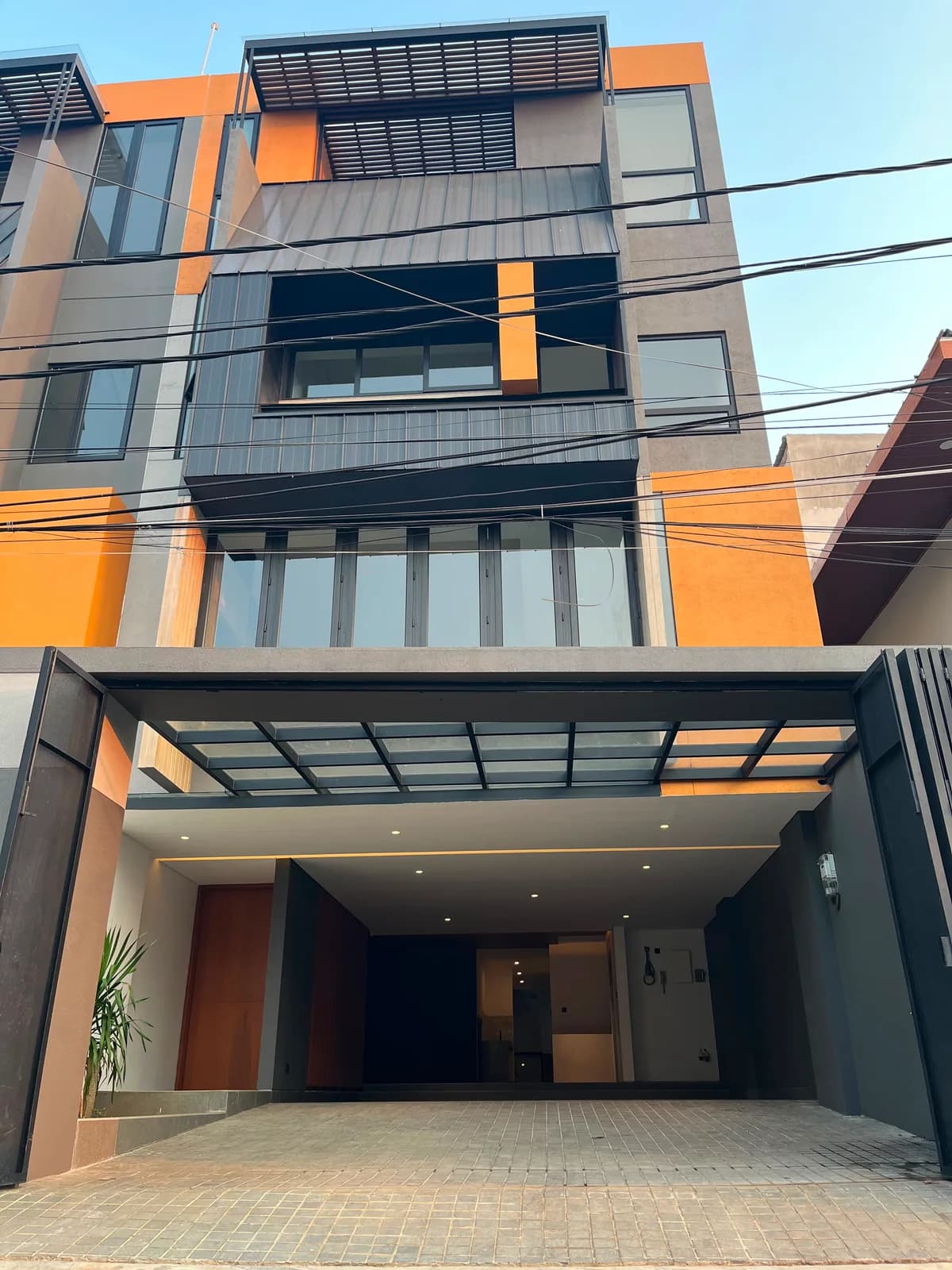 The house photographed straight on from the street, four storeys of grey, orange and timber