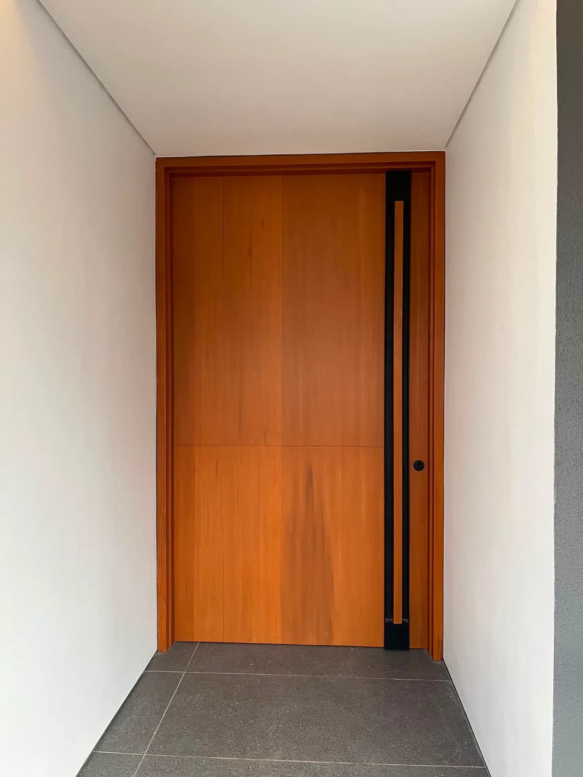 The timber pivot front door with a full-height black handle, set in a white entrance recess
